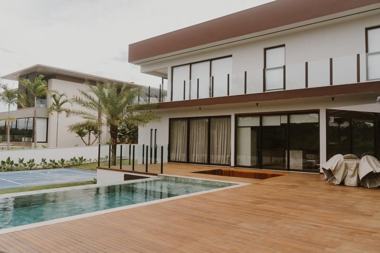 Fachada posterior de residência de dois pavimentos com piscina, deck de madeira e palmeiras